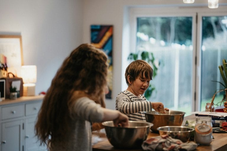 Ein kleiner Junge und ein Mädchen mischen Zutaten in großen Schüsseln auf einer Küchentheke und haben Spaß daran, gemeinsam in einem hellen, gemütlichen Raum mit einem Fenster zu backen, während sie darüber diskutieren, ihrem Rezept Nahrungsergänzungsmittel hinzuzufügen.